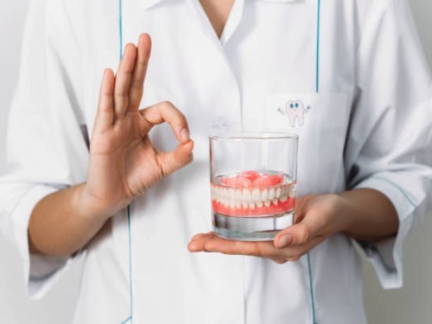 An orthopedic dentist shows how to take care of dentures, close-up. Dental implant care. A complete removable denture in the hands of a doctor. Oral hygiene. Copy space
